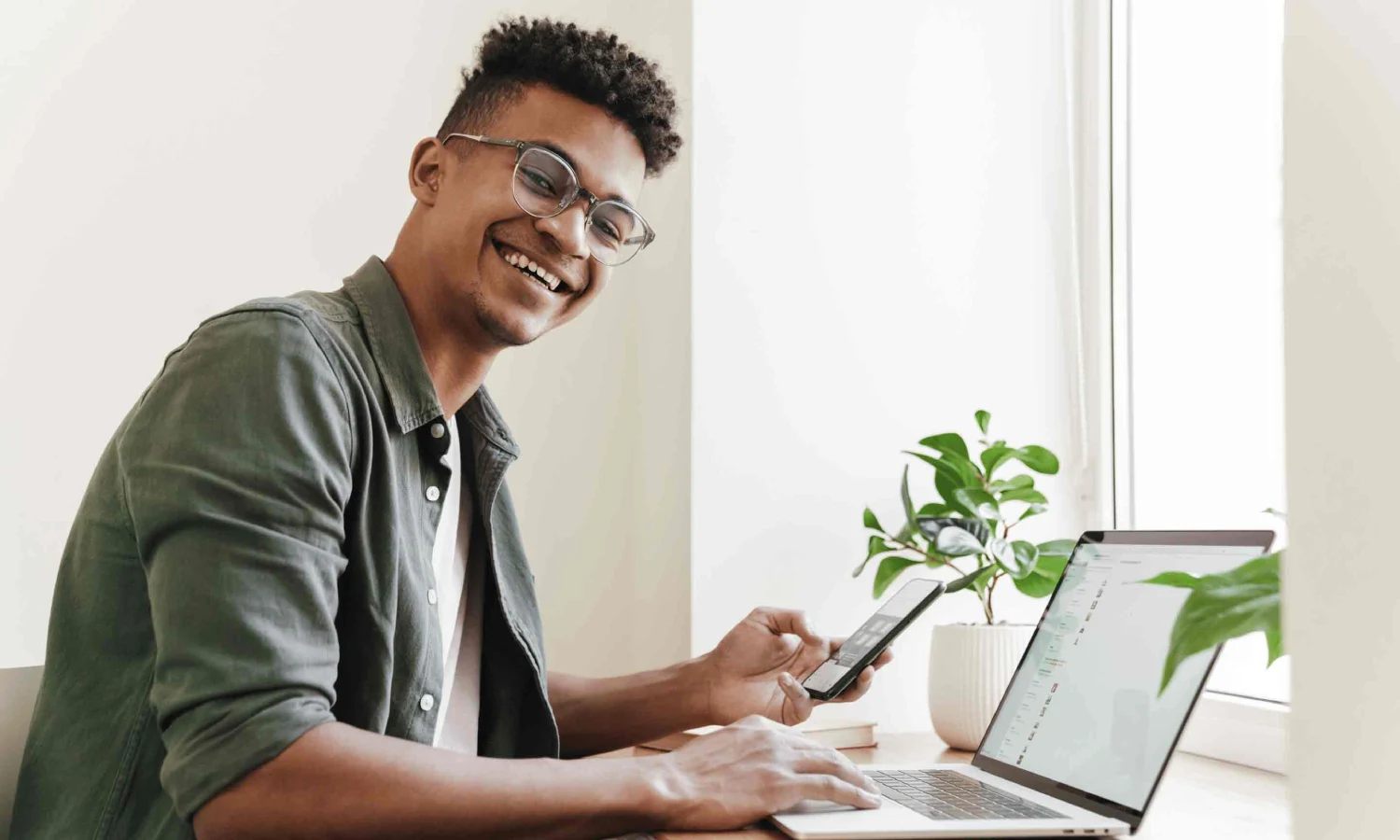 Blije man achter zijn bureau aan het thuiswerken met laptop en telefoon